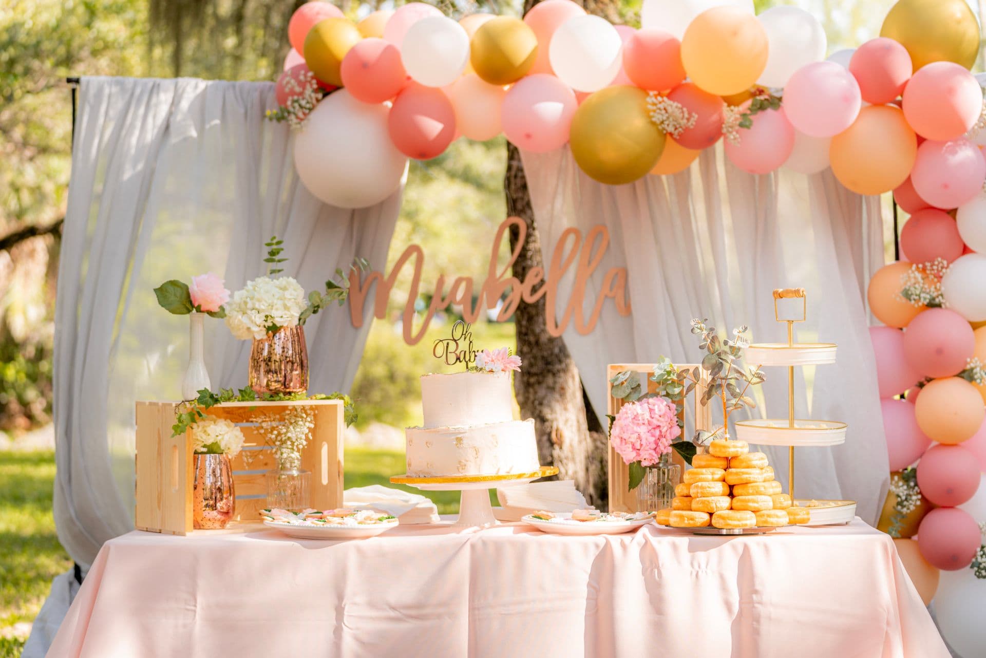 Elegant outdoor baby shower dessert table with a peach and gold balloon garland